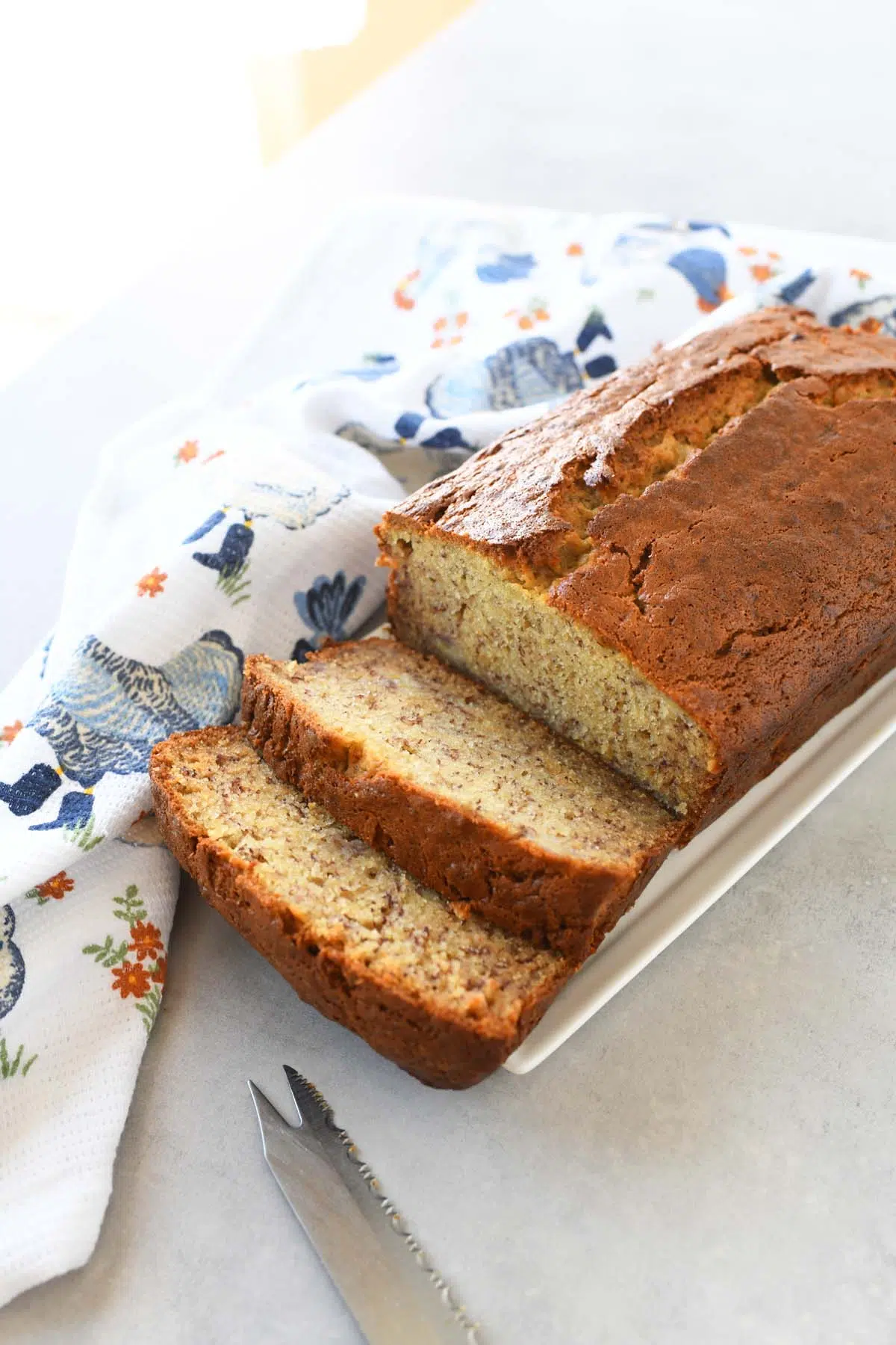 Sliced sour cream banana bread on a white plate near a blue chicken napkin.