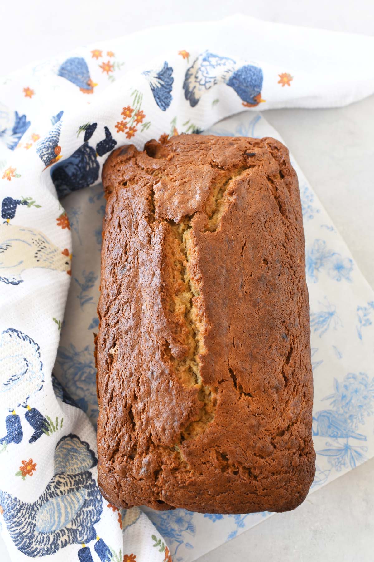 Baked sour cream banana bread near a blue chicken dish towel.