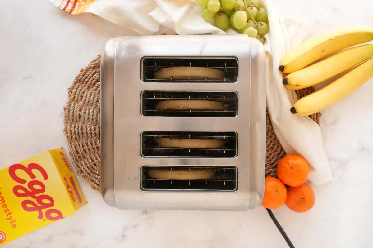 A silver four spot toaster with Eggo Waffles inside and near fresh fruits.