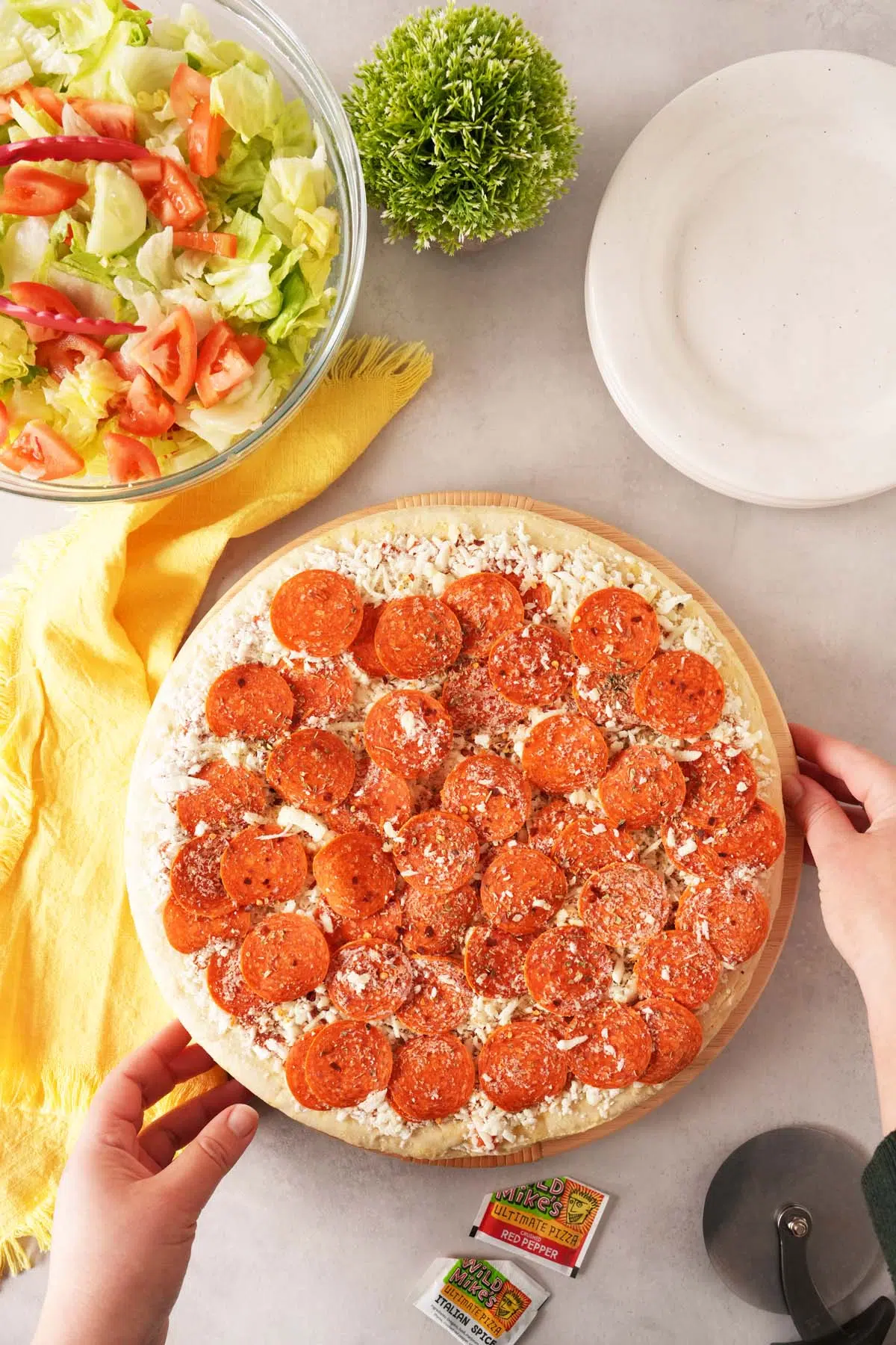 Unbaked, peperoni-loaded Wild Mike's Pizza on a grey table.