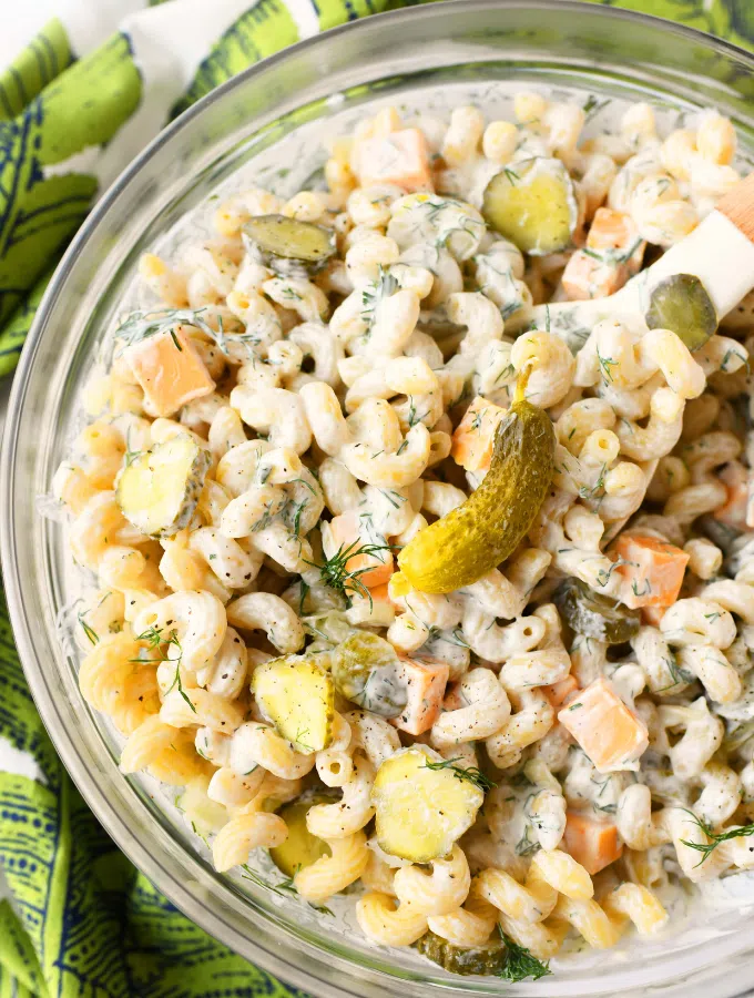 A glass bowl loaded with dill pickle pasta salad with a green printed napkin nearby.