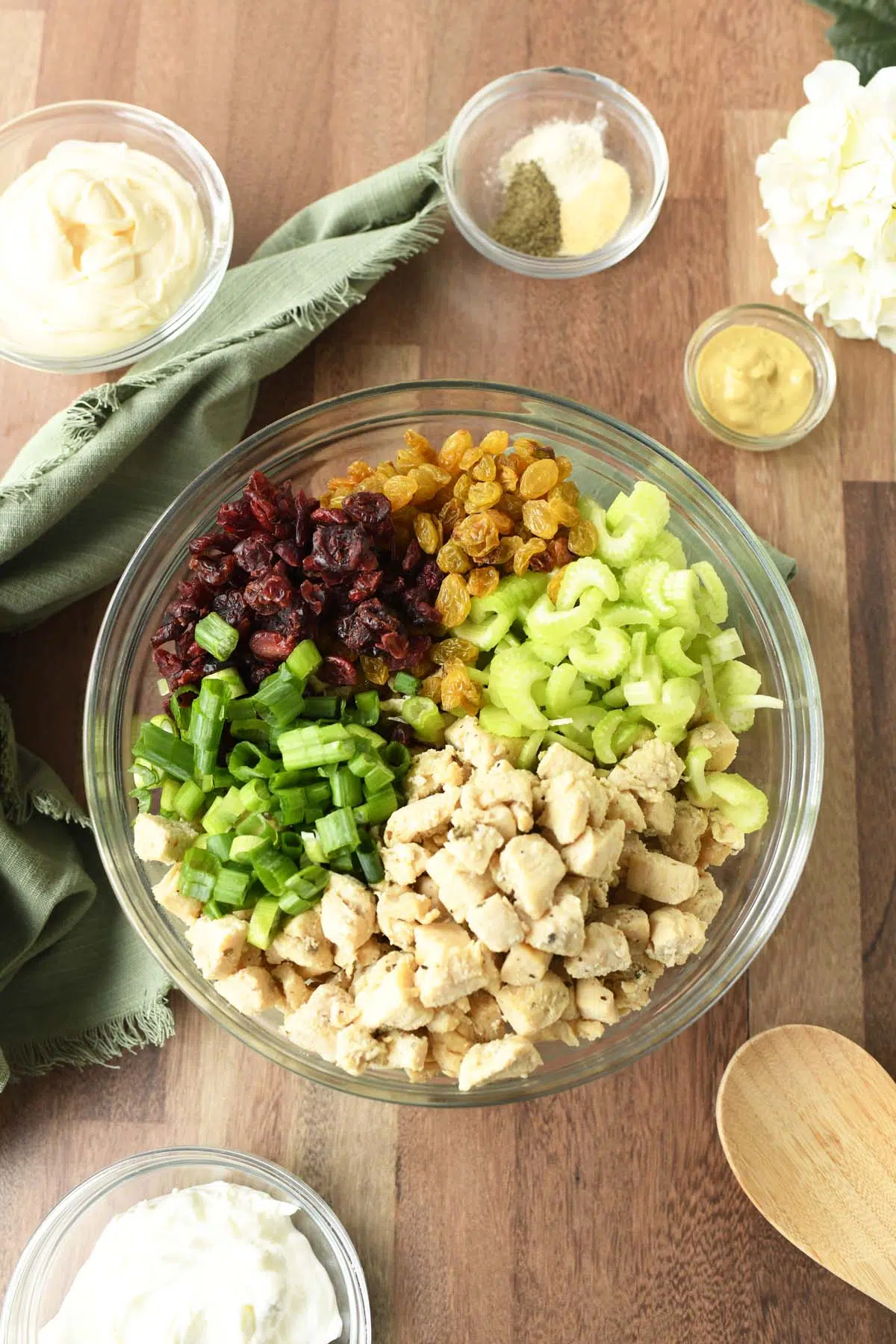 A colorful, glass bowl full of ingredients on a wooden table bear other ingredient dishes.