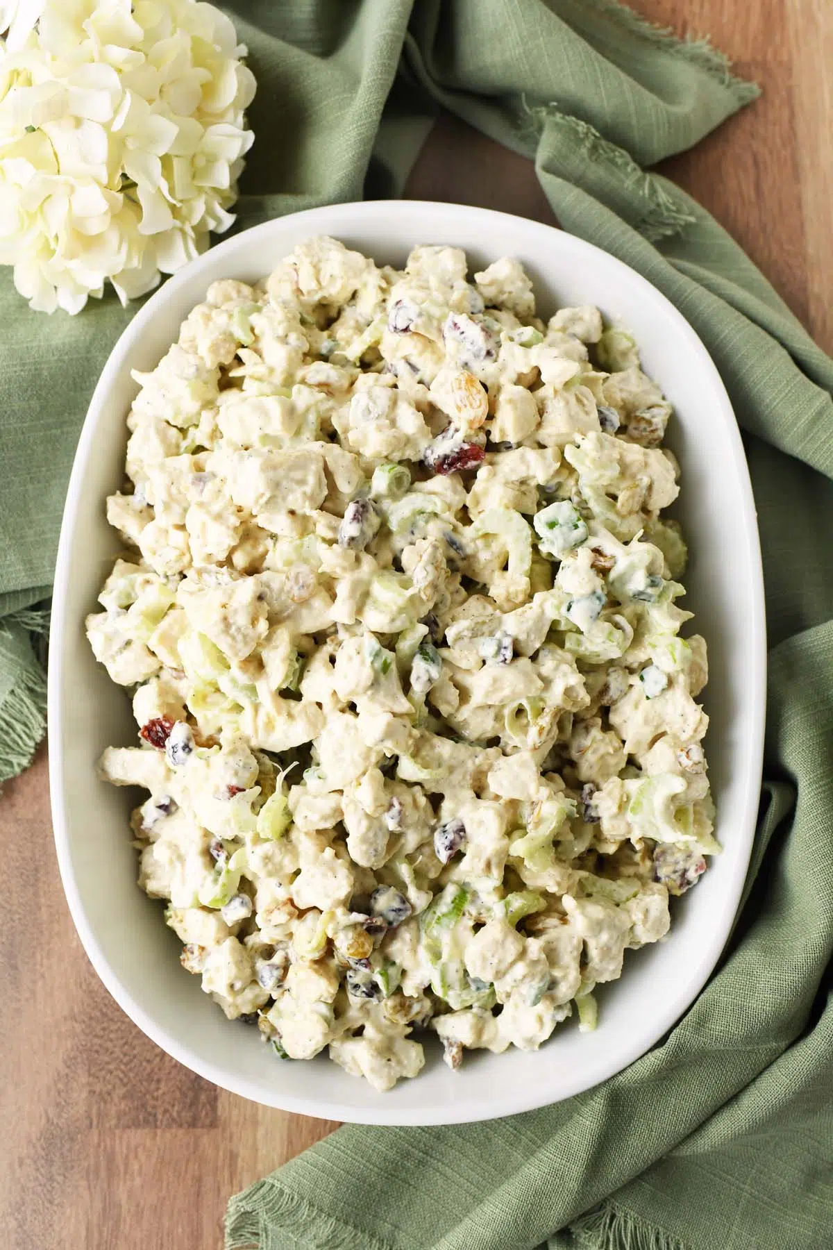 Harvest chicken salad in a white dish near green napkins and a white flower.