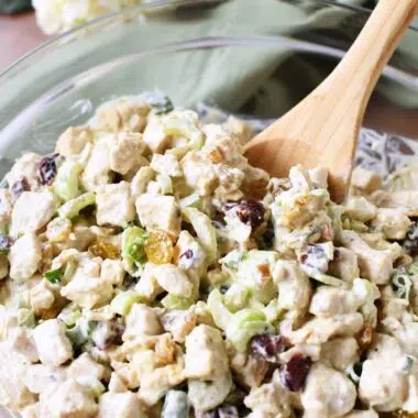 A wooden spoon inside roasted chicken salad in a glass bowl.