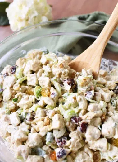 A wooden spoon inside roasted chicken salad in a glass bowl.