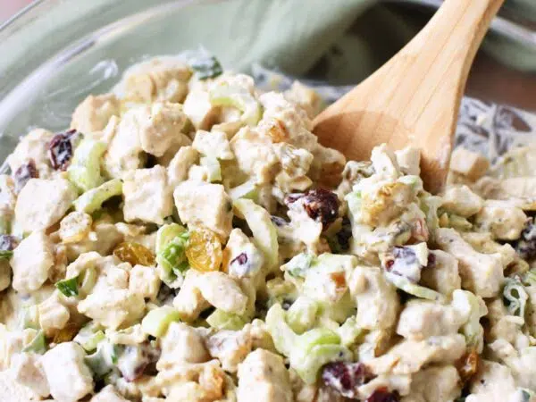 A wooden spoon inside roasted chicken salad in a glass bowl.