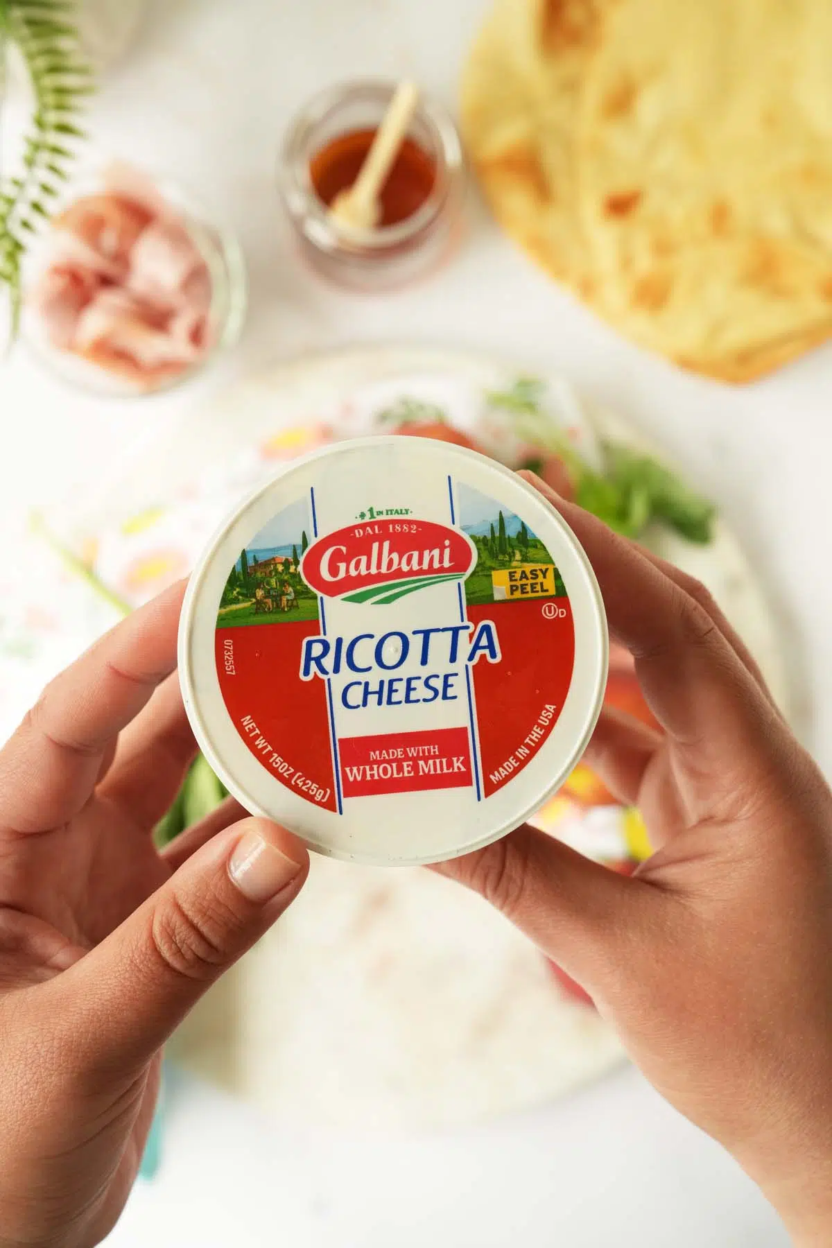 Hands holding up the top of a container of Galbani Ricotta.
