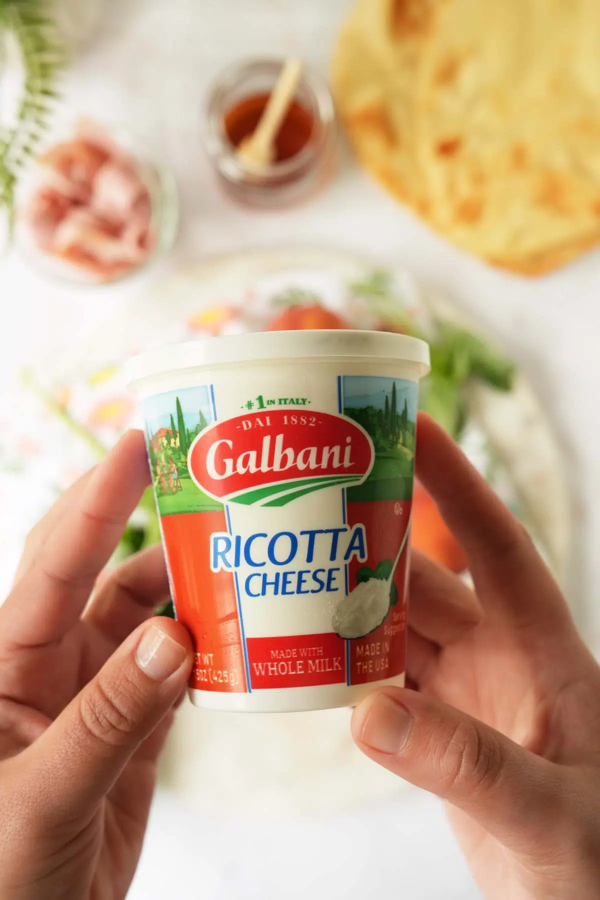 Hands holding up a container of Galbani Whole Milk Ricotta Cheese.
