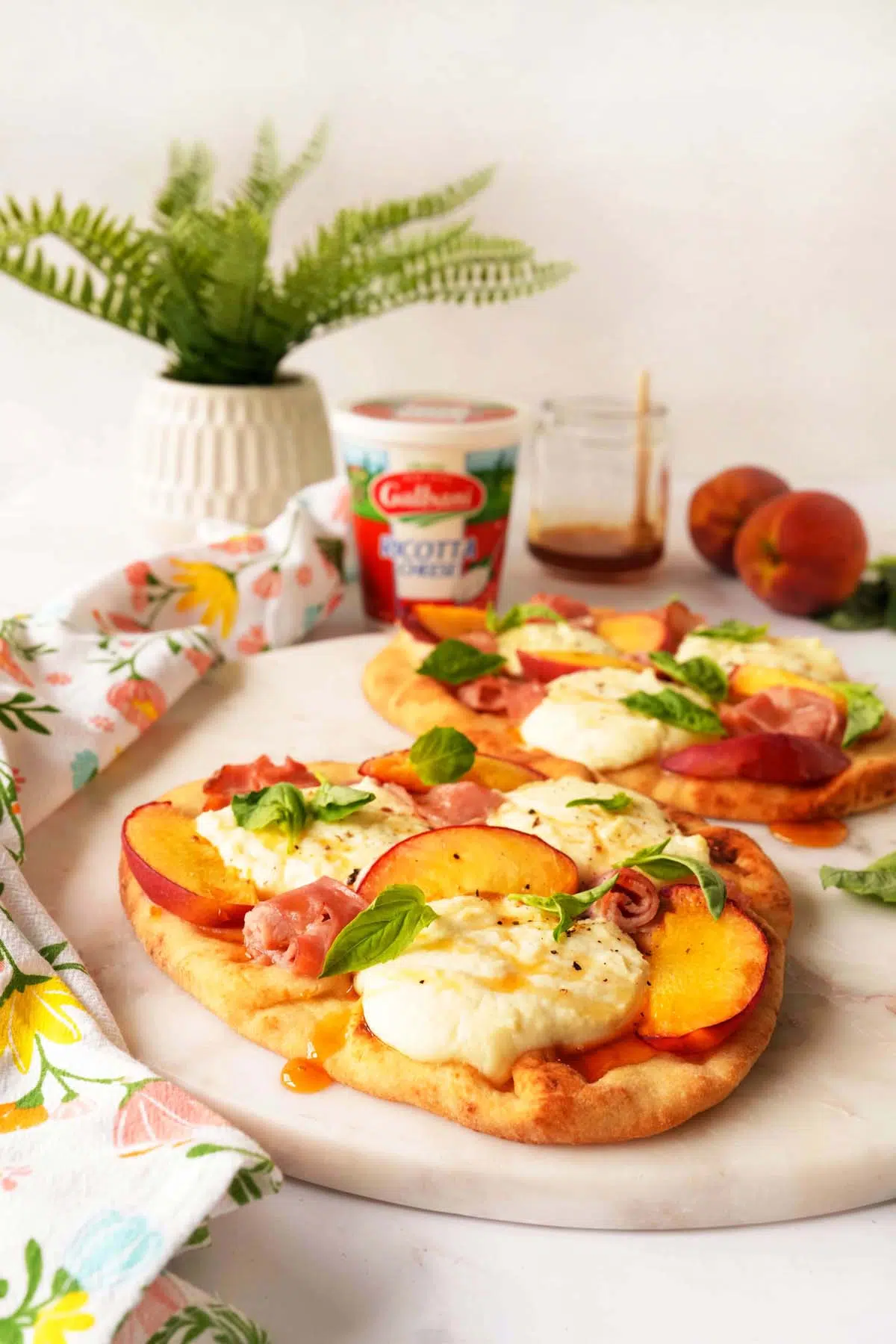 A shot of vibrant peach hot honey ricotta flabreads near a green plant, and container of Galbani Ricotta.
