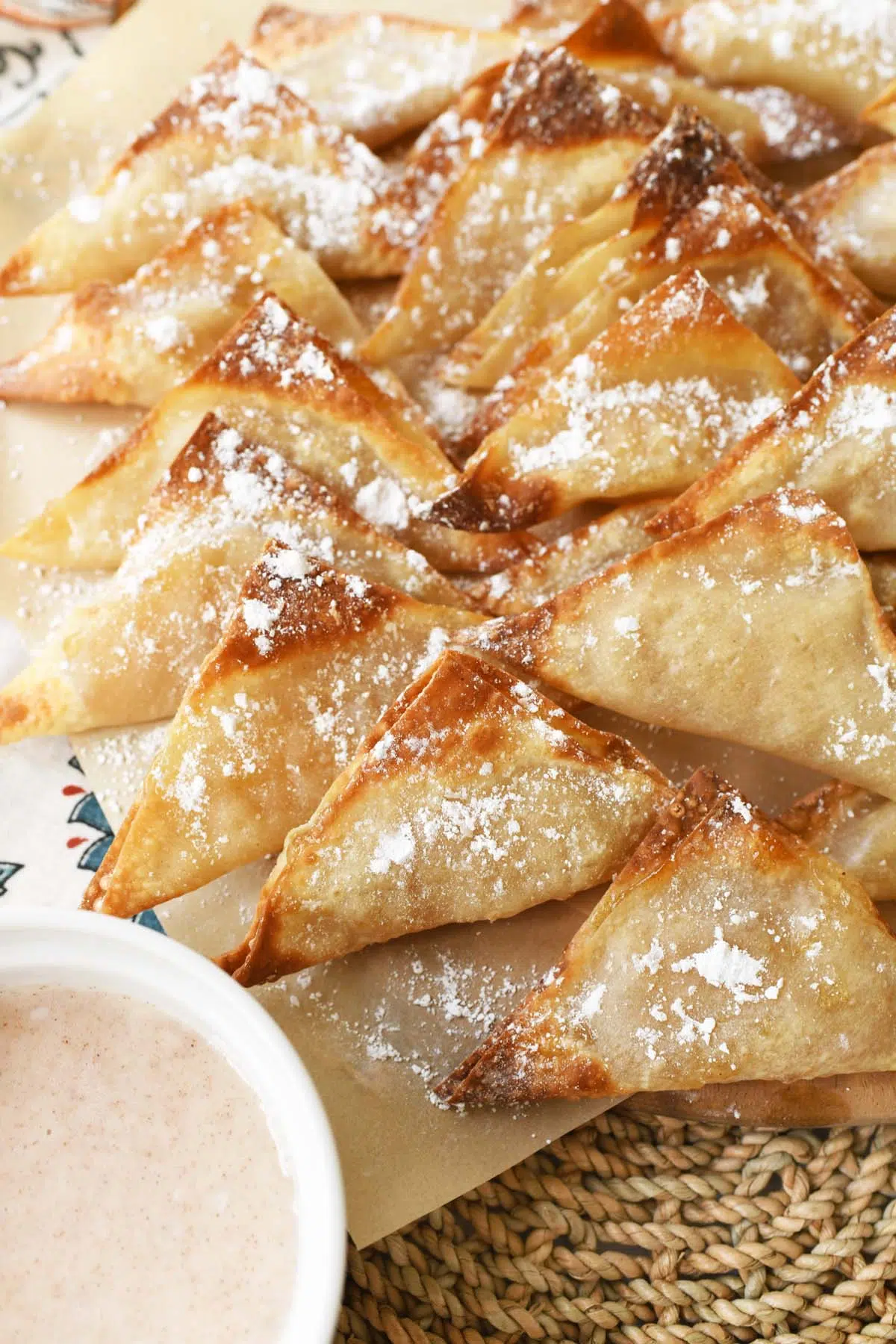 A platter of air fried, golden-brown apple pie wontons on a straw placemat.