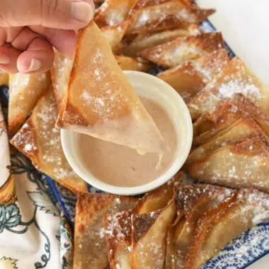 A hand holding a golden-brown apple pie wontons that is dripping with icing.