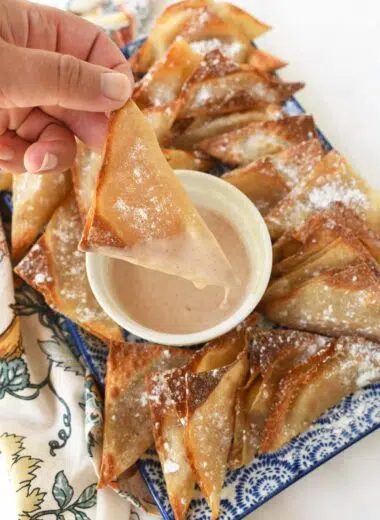 A hand holding a golden-brown apple pie wontons that is dripping with icing.