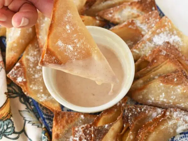 A hand holding a golden-brown apple pie wontons that is dripping with icing.