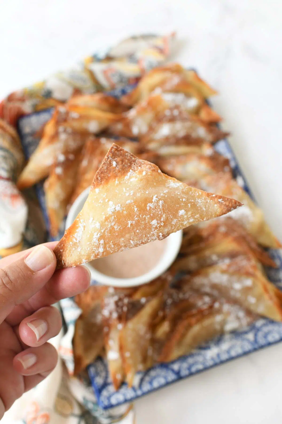 A hand holding up a crispy, apple pi wonton.