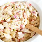 A wooden spoon inside a white bowl of crab pasta salad.