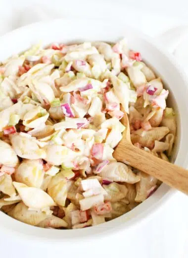 A wooden spoon inside a white bowl of crab pasta salad.