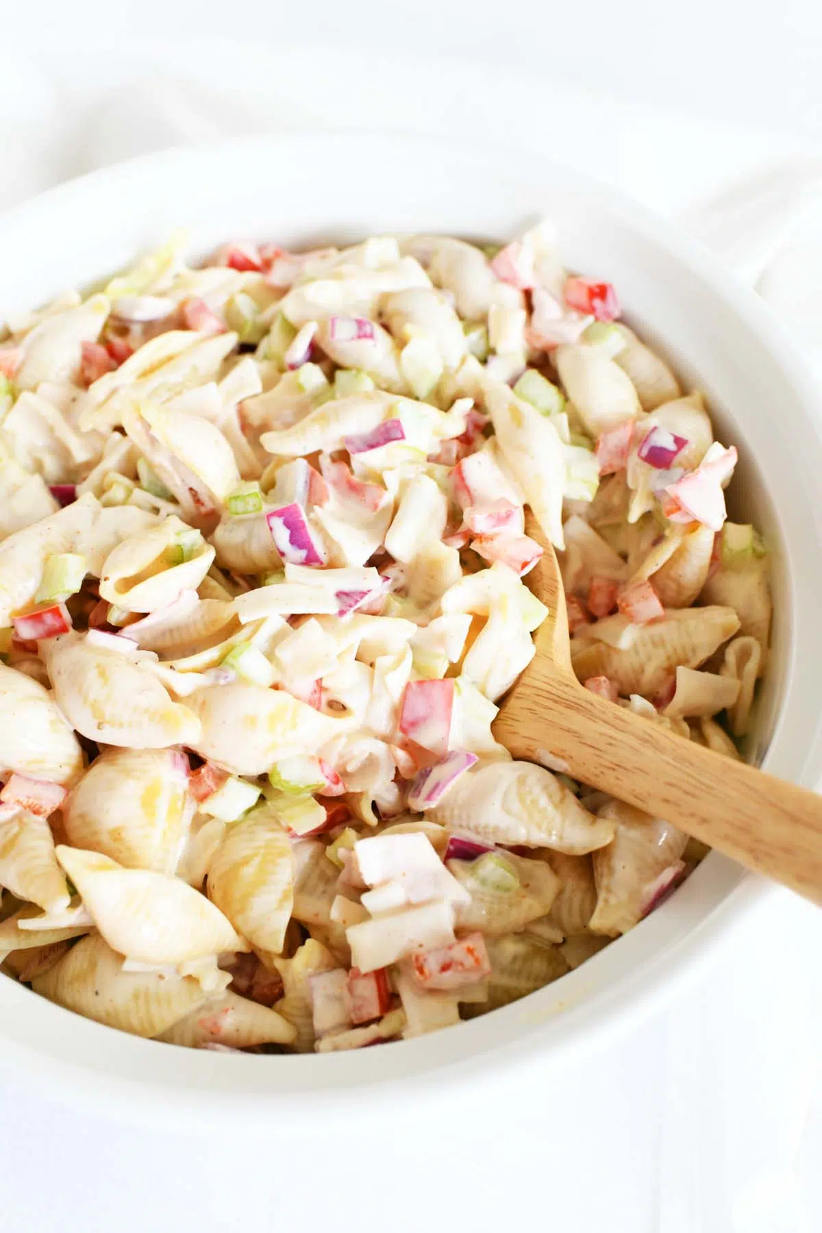 A wooden spoon inside a white bowl of crab pasta salad.