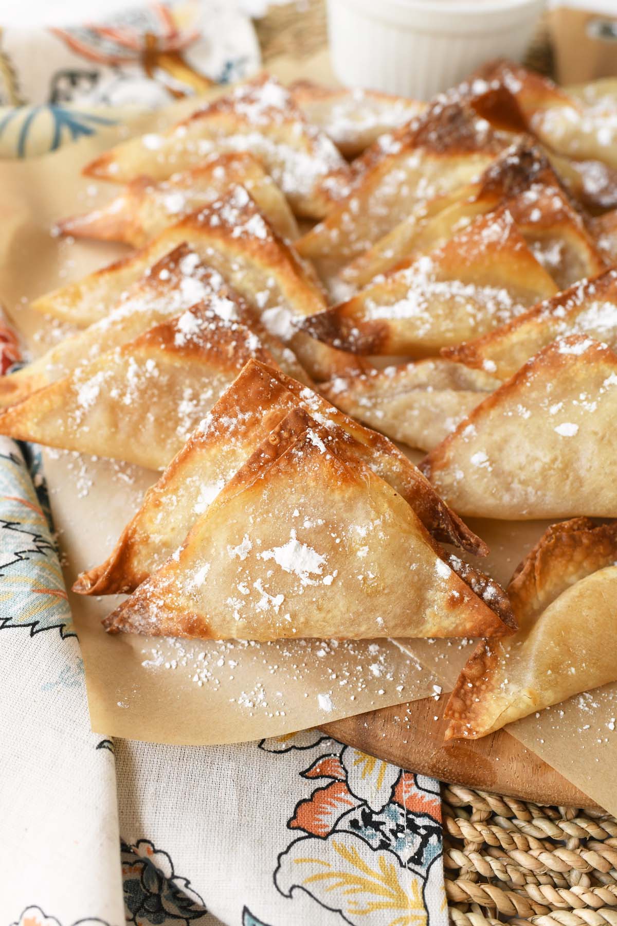 Golden-Brown, crispy apple pie wontons on a platter near a patterned napkin.