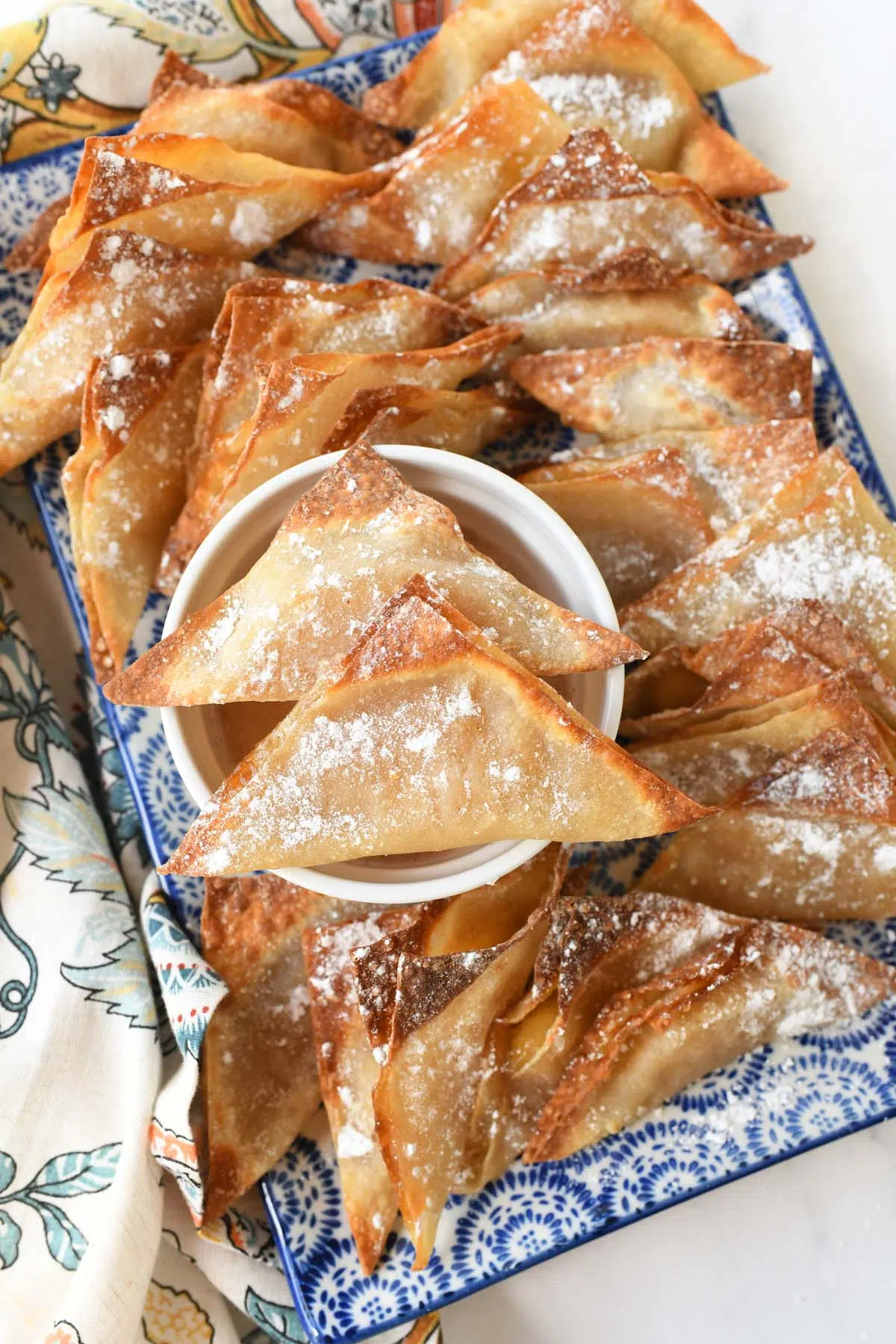 Crispy apple pie wontons on a blue patterned platter.