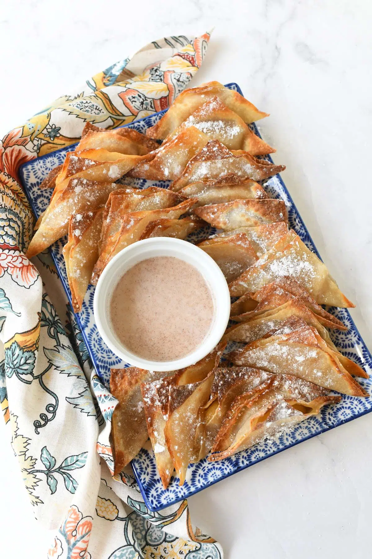 Golden Brown apple pie wontons on a blue, patterned plate with cinnamon icing.