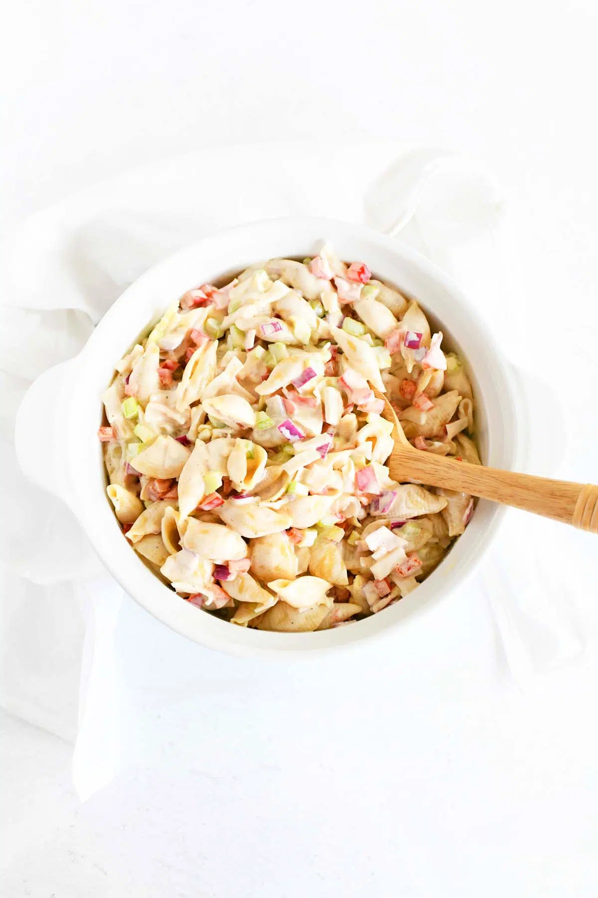 Crab pasta salad inside a white bowl with a wooden spoon.