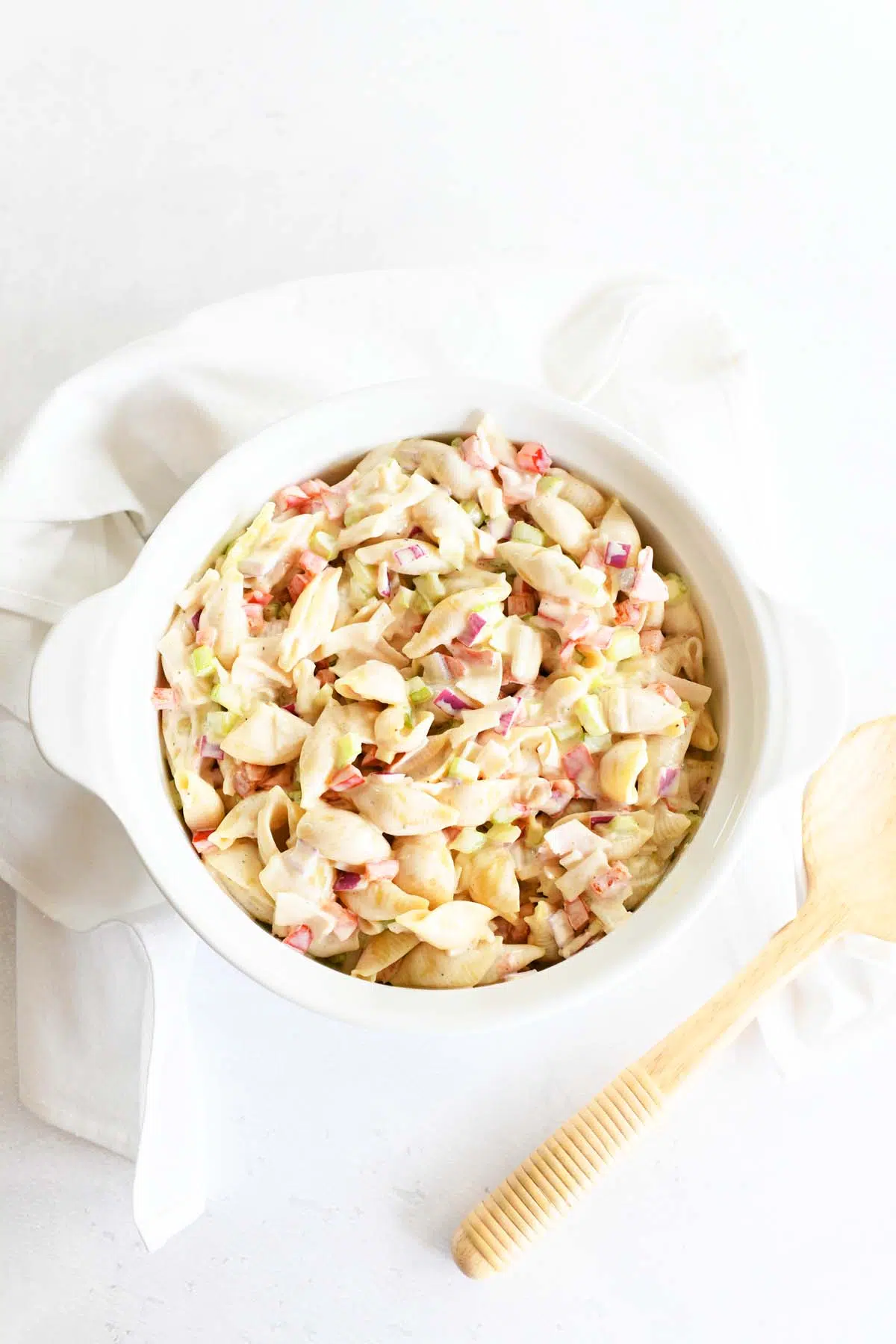 A white bowl of crab pasta salad near a white napkin and wooden spoon.