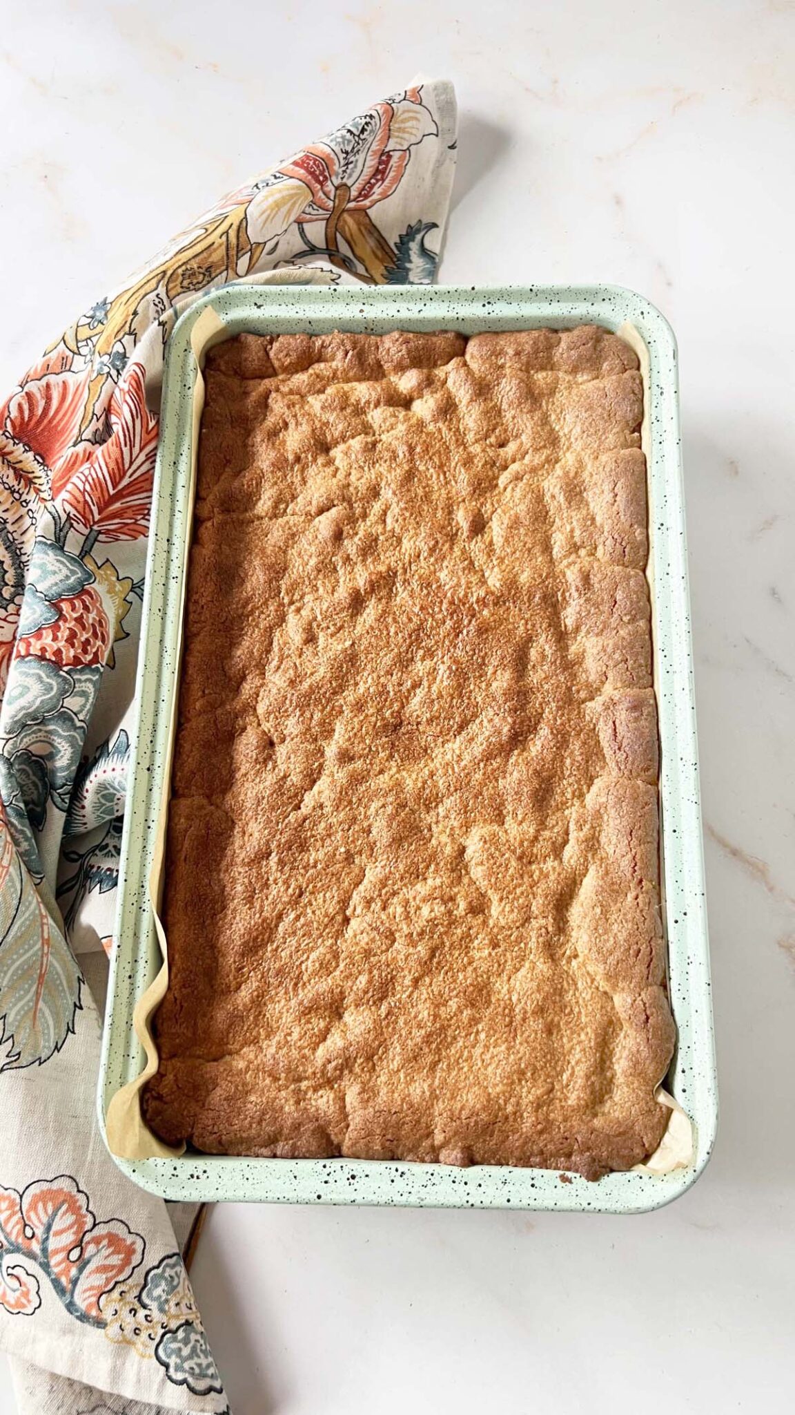 Golden brown baked peanut butter blondies in a blue pan with a floral napkin nearby.