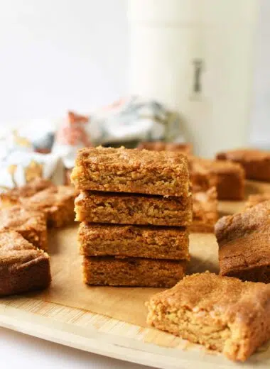 A stack on peanut butter blondies in a wooden cutting board with a white jar and floral napkin in the background.