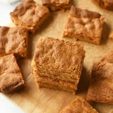 Golden-brown peanut butter blondies cut and some stacked on a brown cutting board.