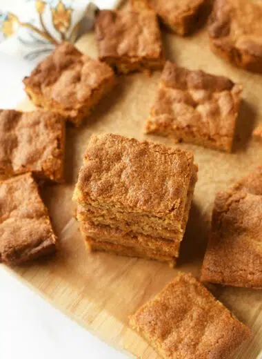 Golden-brown peanut butter blondies cut and some stacked on a brown cutting board.